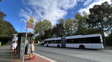 Auberg bus stop in Kiel, where a woman is waiting and a white bus is seen in the other side of the road